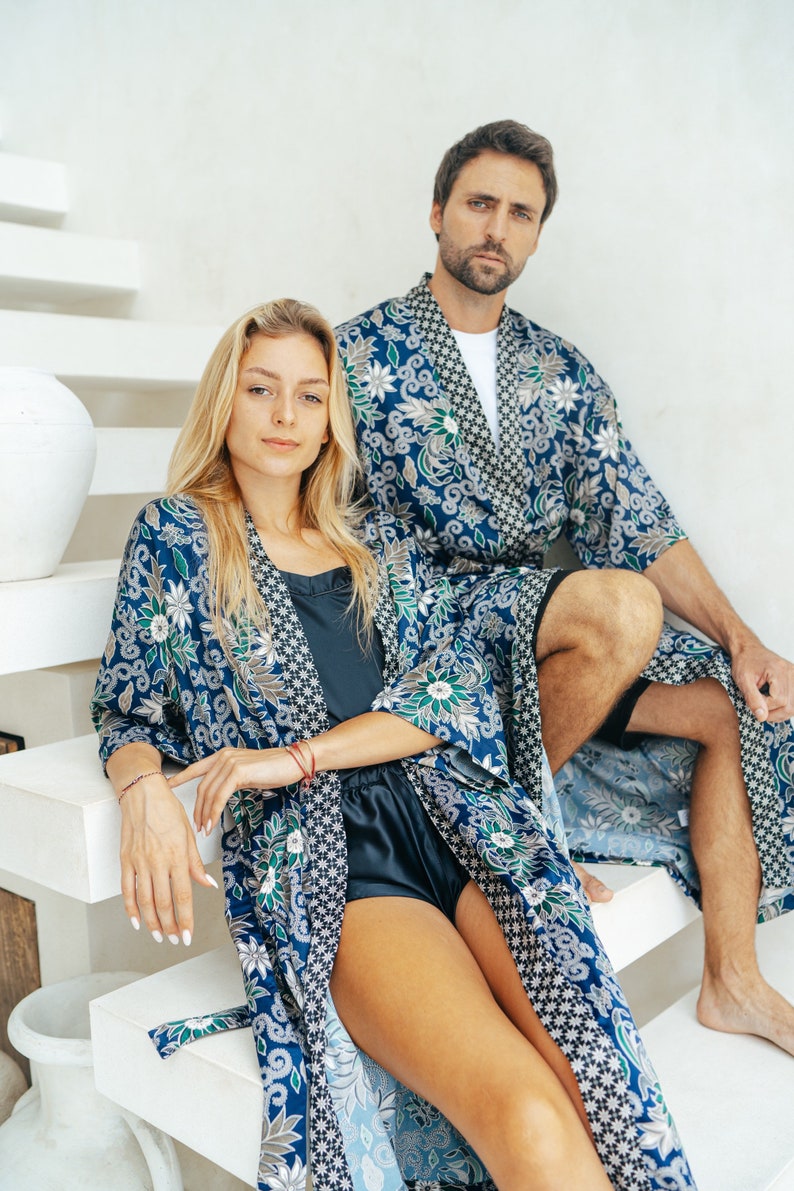 May include: A couple wearing matching blue and green floral patterned robes. The robes have a black trim and are tied at the waist. The couple is sitting on a white staircase.