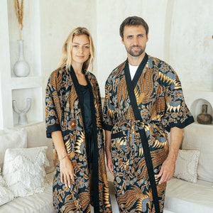 Könnte beinhalten: Ein Paar trägt passende schwarze und goldfarbene Roben mit blauem Blumendesign. Die Roben haben einen schwarzen Saum und eine Schärpe.