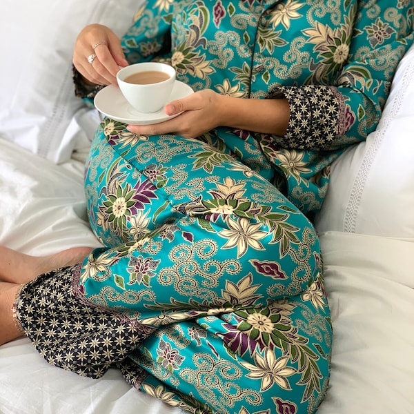 May include: A teal blue and gold floral patterned pajama set with black trim. The pajama top has a collar and long sleeves. The pajama pants have a wide leg.