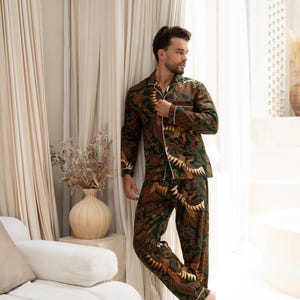 Puede incluir: Conjunto de pijama con estampado verde y marr&oacute;n con ribete blanco. La parte superior de manga larga y los pantalones presentan un dise&ntilde;o repetitivo. El pijama est&aacute; hecho de un material suave. El modelo est&aacute; cerca de una ventana.