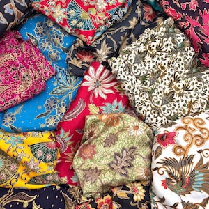 May include: A collection of colorful batik fabrics with intricate floral and geometric patterns. The fabrics feature a variety of colors, including red, blue, yellow, and green. The designs include flowers, leaves, and abstract shapes.