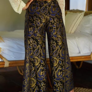 May include: Black wide-leg pants with a blue and gold floral pattern. The pants have a high waist and a loose fit.