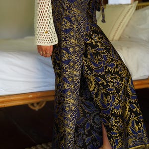 May include: A long, flowing skirt with a black background and a blue and gold patterned design. The skirt has a side slit and a tie at the waist.