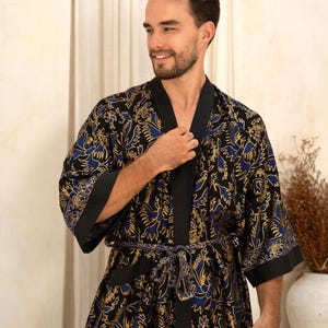 May include: A black kimono-style robe with a floral pattern in gold and blue. The robe has black trim on the collar, sleeves, and belt. The robe is tied at the waist with a matching belt.