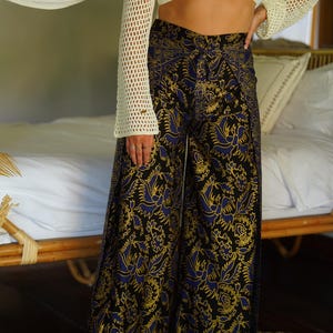 May include: Wide-leg pants with a black background and a blue and gold floral pattern. The pants have a high waist and a relaxed fit.