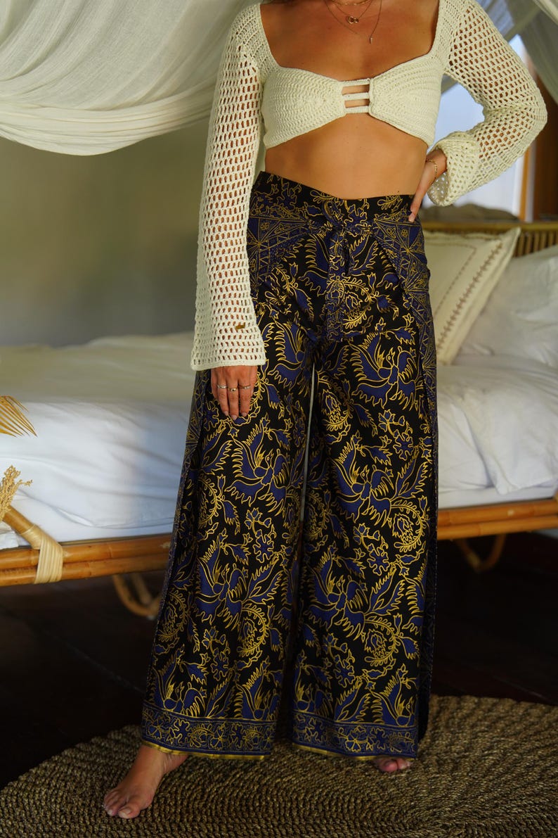 May include: Wide-leg pants with a black background and a blue and gold floral pattern. The pants have a high waist and a relaxed fit.