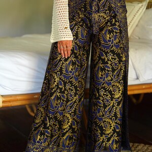 May include: Wide-leg pants with a black background and a blue and gold floral pattern. The pants have a tie at the waist and a slit on each side.
