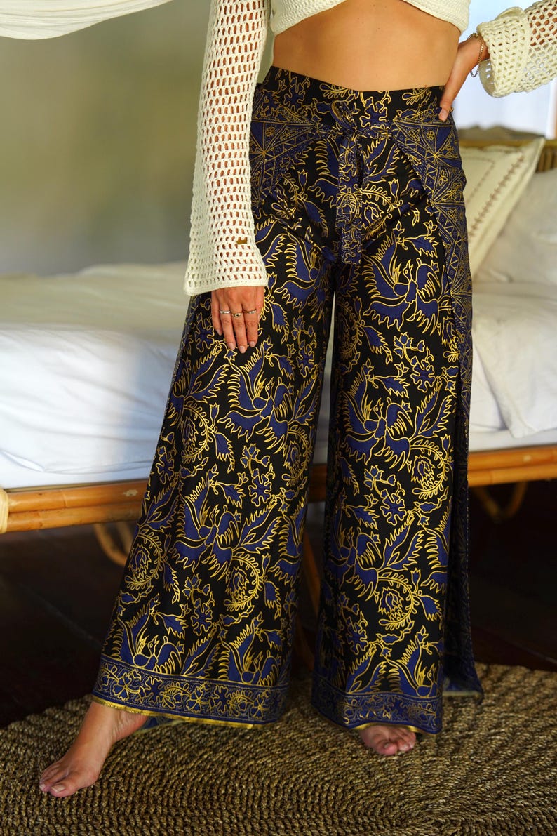 May include: Wide-leg pants with a black background and a blue and gold floral pattern. The pants have a tie at the waist and a slit on each side.