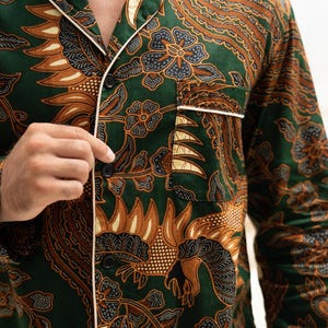 Puede incluir: Camisa de pijama verde con un estampado floral marr&oacute;n y negro. La camisa de manga larga tiene ribetes blancos en el cuello, los pu&ntilde;os y el bolsillo. Tiene botones negros en la parte delantera.