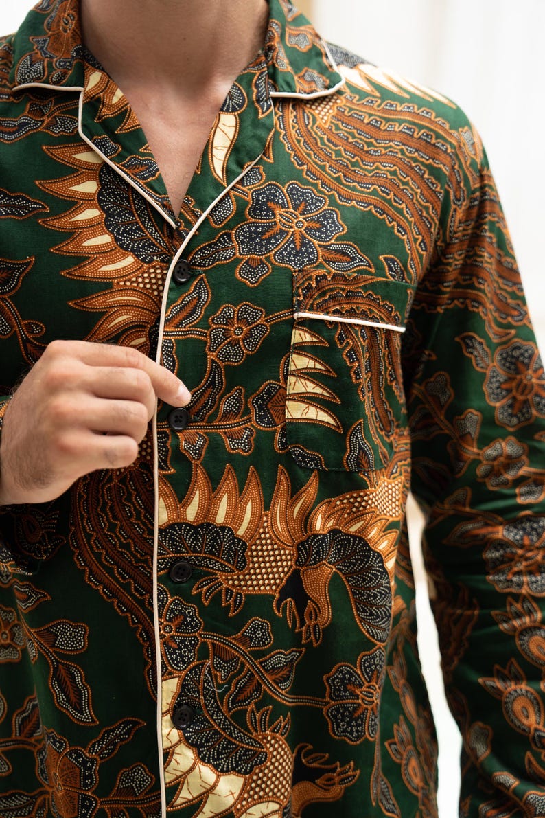 Puede incluir: Camisa de pijama verde con un estampado floral marr&oacute;n y negro. La camisa de manga larga tiene ribetes blancos en el cuello, los pu&ntilde;os y el bolsillo. Tiene botones negros en la parte delantera.