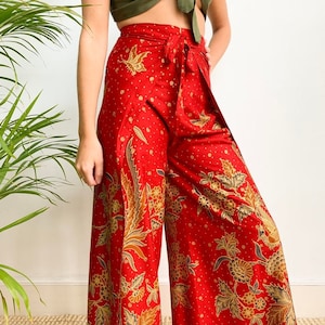 Può includere: Pantaloni larghi rossi con stampa floreale e vita con lacci. I pantaloni sono realizzati in tessuto setoso e hanno una vestibilità rilassata.