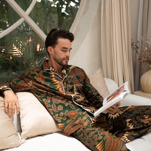 Puede incluir: Conjunto de pijama con estampado verde y marr&oacute;n con ribete blanco. La ropa de dormir de dos piezas presenta una camisa con botones y pantalones a juego. El pijama tiene un dise&ntilde;o floral y de cachemira. La persona est&aacute; sentada en un sof&aacute; blanco y leyendo un libro.