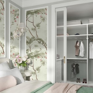 May include: A bedroom with a floral wallpaper design, a white bed, and a built-in closet. The wallpaper features a botanical print with green leaves and pink flowers. The bed has white pillows and a pink and green comforter. The closet has hanging clothes.