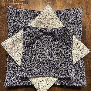 May include: A square fabric bowl cozy featuring a navy blue background with a white swirling vine pattern on the exterior and a white background with a navy blue swirling vine pattern on the interior, constructed with quilted stitching.