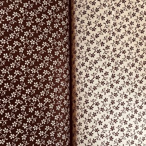 May include: Two pieces of fabric displayed side by side. The left piece is dark brown with a repeating pattern of small white flowers and curved lines. The right piece is cream-colored with a repeating pattern of small dark brown flowers.