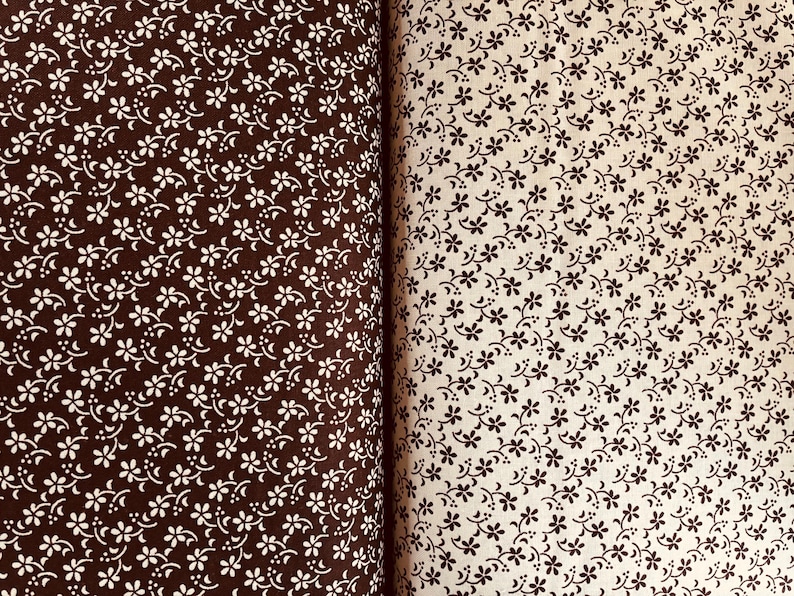 May include: Two pieces of fabric displayed side by side. The left piece is dark brown with a repeating pattern of small white flowers and curved lines. The right piece is cream-colored with a repeating pattern of small dark brown flowers.