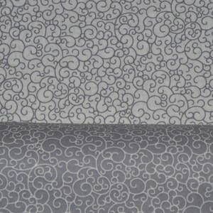 May include: A bolt of fabric featuring a repeating pattern of dark gray swirling lines on a light gray background. The material is folded over, showing the same intricate, continuous scrollwork design on both the flat and curved surfaces.