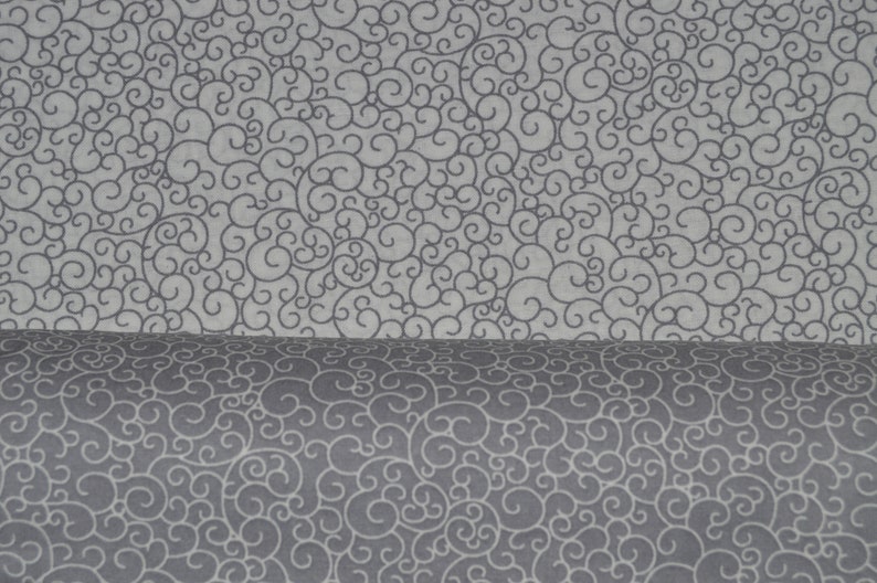 May include: A bolt of fabric featuring a repeating pattern of dark gray swirling lines on a light gray background. The material is folded over, showing the same intricate, continuous scrollwork design on both the flat and curved surfaces.