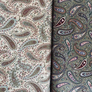 May include: Two pieces of fabric featuring a dense paisley pattern. The left side displays a cream background with muted green, brown, and blue paisley motifs. The right side shows an olive green background with dark brown, blue, and white paisley designs.