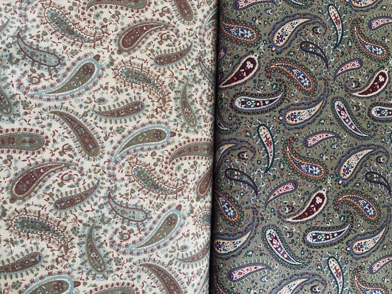 May include: Two pieces of fabric featuring a dense paisley pattern. The left side displays a cream background with muted green, brown, and blue paisley motifs. The right side shows an olive green background with dark brown, blue, and white paisley designs.