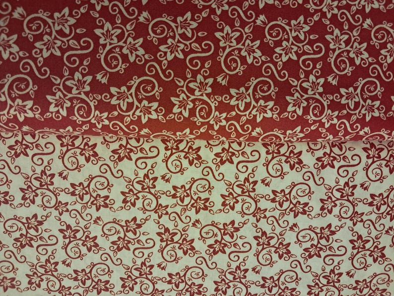 May include: Two folded layers of fabric featuring a repeating floral vine pattern. The top layer is deep red with white floral motifs, while the bottom layer is off-white with deep red floral motifs, both displaying identical swirling leaf designs.