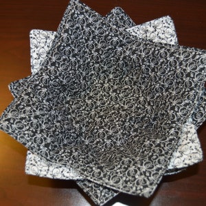 May include: A fabric bowl cozy featuring a black and white floral scroll pattern. The square-shaped holder has eight pointed corners and is constructed with quilted fabric, showcasing a contrasting black interior and a white exterior design.
