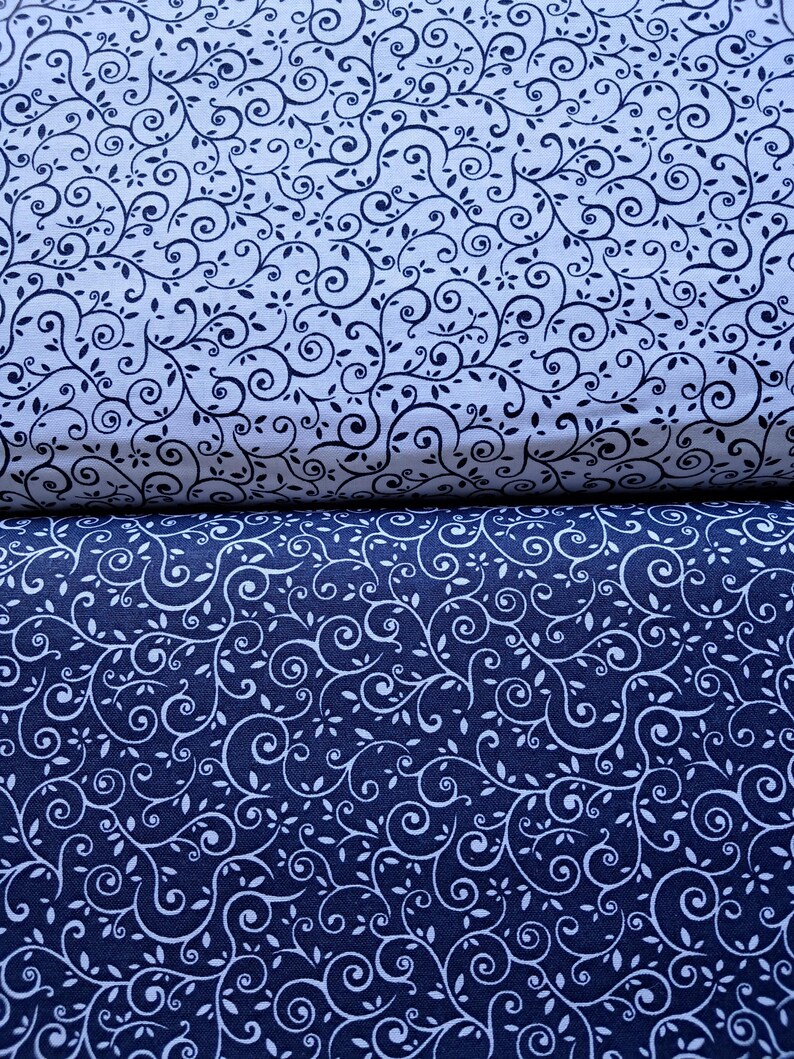 May include: Two folded pieces of fabric featuring a continuous scrolling vine and leaf pattern. The top fabric is white with dark navy blue lines, while the bottom fabric is dark navy blue with white lines, creating a contrasting color scheme.