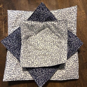May include: Two square fabric bowl cozies featuring a navy blue and white swirling vine pattern. The larger cozy has a white background with navy vines, while the smaller nested cozy has a navy background with white vines, both quilted.