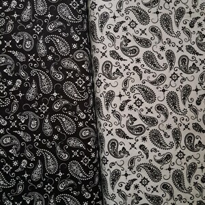 May include: Two rolls of fabric featuring a repeating paisley pattern. The left roll is black with a white print, while the right roll is white with a black print. Both textiles display intricate teardrop shapes and small floral accents throughout.