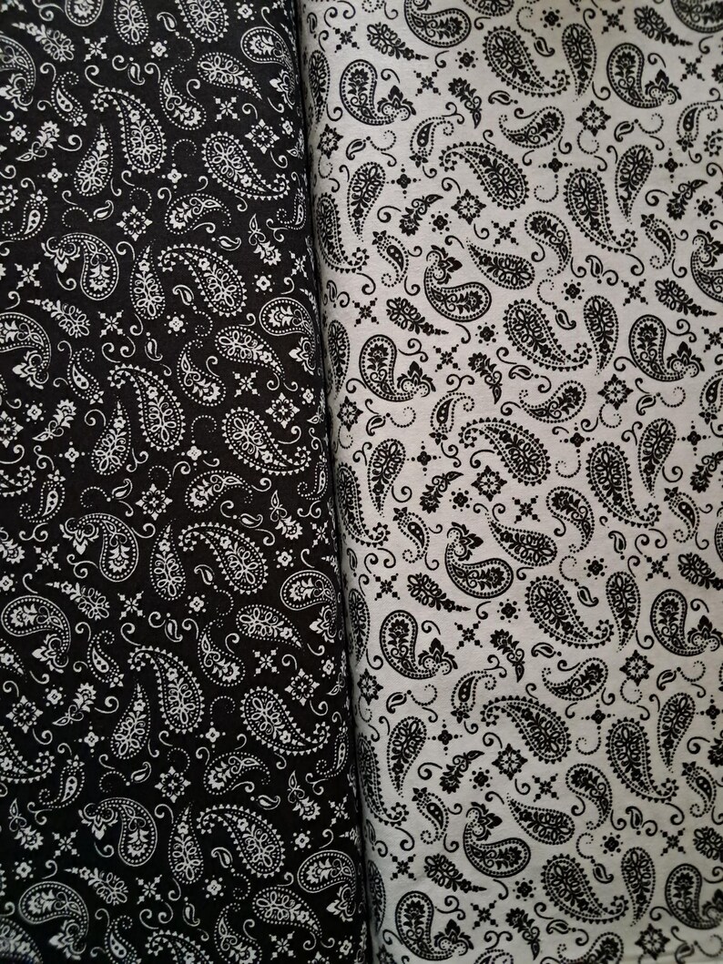 May include: Two rolls of fabric featuring a repeating paisley pattern. The left roll is black with a white print, while the right roll is white with a black print. Both textiles display intricate teardrop shapes and small floral accents throughout.
