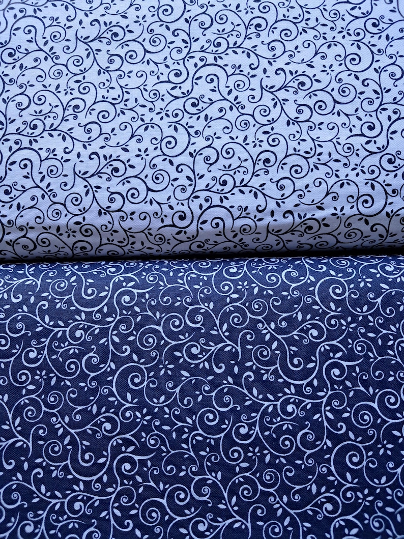 May include: Two folded pieces of fabric featuring a continuous scrolling vine and leaf pattern. The top fabric is white with dark navy blue lines, while the bottom fabric is dark navy blue with white lines, creating a contrasting color scheme.