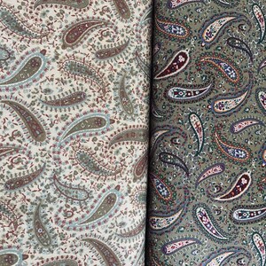 May include: Two pieces of fabric featuring a dense paisley pattern. The left side displays a cream background with muted green, brown, and blue paisley motifs. The right side shows an olive green background with dark brown, blue, and white paisley designs.