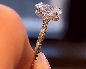 May include: A gold ring with a large, clear, oval-cut diamond as the centerpiece. The diamond is surrounded by smaller accent stones. The ring is held up, showcasing the intricate details of the setting and the brilliance of the gemstones.