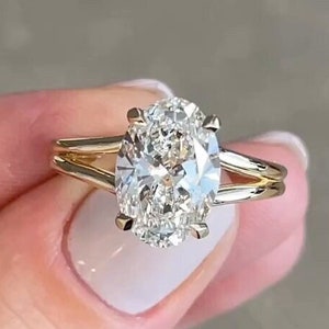 Puede incluir: Un anillo de compromiso de oro con un gran diamante de forma ovalada. El anillo tiene un diseño de doble banda.