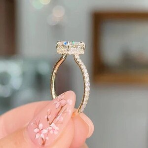 May include: A gold engagement ring with a large, oval-shaped center stone surrounded by smaller diamonds. The band is also set with diamonds.