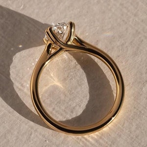 May include: A gold engagement ring with a single round diamond set in a delicate, twisted band.