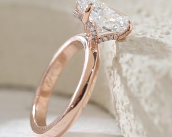 May include: Rose gold engagement ring featuring a pear-shaped diamond. The ring has a delicate band and small accent diamonds around the main stone. The setting is a classic design, showcasing the brilliance of the diamond.