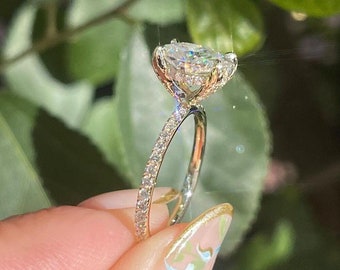 Könnte beinhalten: Ein goldener Verlobungsring mit einem großen ovalen Diamanten, der in einer Krappenfassung sitzt. Die Band ist eine dünne Pavé-Band mit kleinen Diamanten.
