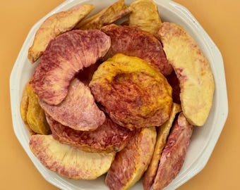 May include: A white bowl filled with dried peach slices. The fruit pieces exhibit a gradient of colors ranging from pale yellow and cream to deep reddish-purple hues. The texture of the dried fruit appears wrinkled and firm, with visible fibrous details.