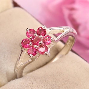May include: A silver ring with a pink flower design. The flower is made of small pink gemstones.