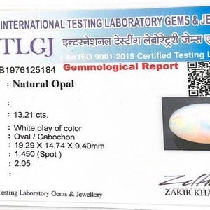 May include: A white gemological report card from International Testing Laboratory Gems & Jewellery for a natural opal. The card displays report number SLB1976125184, a QR code, a photo of an oval cabochon opal, and technical data including 13.21 cts weight.