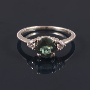 May include: A silver ring with a large, round, dark green gemstone surrounded by two smaller, round, white gemstones.