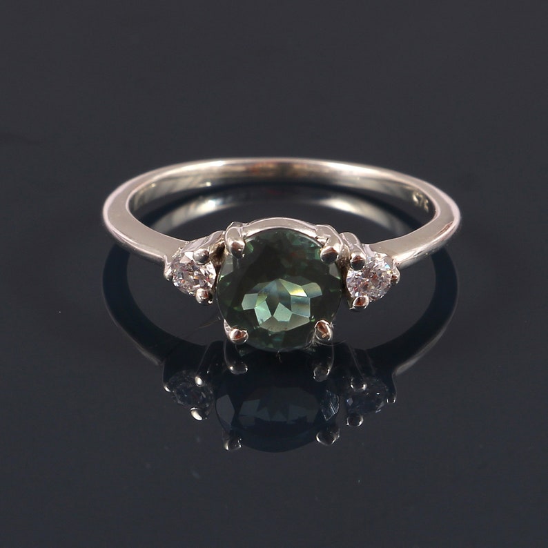 May include: A silver ring with a large, round, dark green gemstone surrounded by two smaller, round, white gemstones.