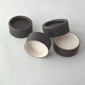 Peut inclure: Quatre boîtes rondes en carton noir avec des intérieurs blancs. Les boîtes sont empilées les unes sur les autres.