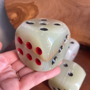 May include: A set of three white marble dice with black and red dots. The dice are stacked on top of each other.