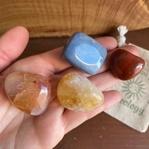 Puede incluir: Cuatro piedras pulidas en una mano. Las piedras son de color azul claro, naranja claro, naranja oscuro y rojo oscuro.