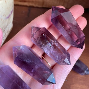 May include: Four amethyst crystal points with a purple hue and iridescent sparkle. The points are double terminated and have a smooth, polished finish.