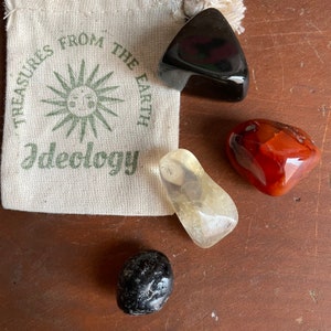 May include: Four tumbled stones in a small pouch. The pouch is made of natural fabric and has the words "Treasures from the Earth Ideology" printed on it. The stones are black obsidian, clear quartz, carnelian, and black onyx.