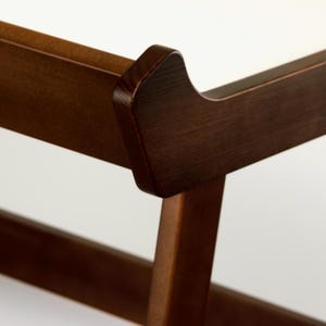 May include: Close-up of a wooden furniture frame, showcasing the joinery and design. The wood has a rich, dark brown finish. The frame's corner features a curved detail, adding a touch of elegance to the piece. The background is a clean white.