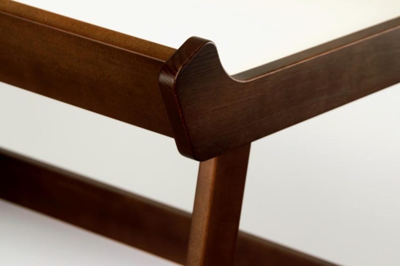 May include: Close-up of a wooden furniture frame, showcasing the joinery and design. The wood has a rich, dark brown finish. The frame's corner features a curved detail, adding a touch of elegance to the piece. The background is a clean white.